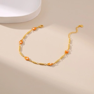 Détail de la chevillère dorée avec breloques Hamsa orange et perles d'œil bleu maléfique