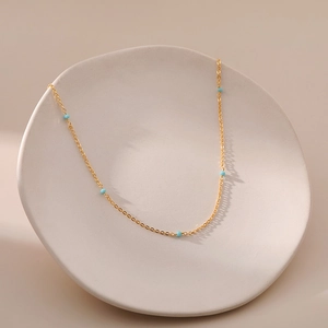 Detailopname van een fijne gouden ketting met kleine turquoise blauwe kralen op tray