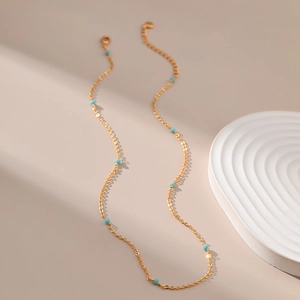 Detail van een dunne 18K vergulde ketting versierd met kleine turkoois blauwe kralen
