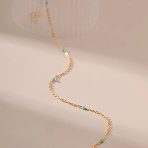 Detail van 18K vergulde ketting met turquoise kralen op een beige achtergrond