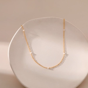 Detail van 18K vergulde minimalistische ketting met vijf kleine witte kralen op dienblad