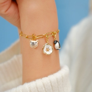 Détail d'un bracelet doré avec breloques en émail : ours polaire, pingouin et fleur