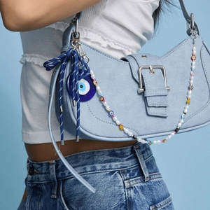 Détail du sac d'épaule en denim bleu clair avec pendentif œil et chaîne de perles