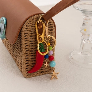 Colorful handmade woven keychain with red pepper charm and beads on a straw bag