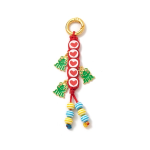 Detail of red braided keychain featuring gold spring clasp with heart beads and frog charms