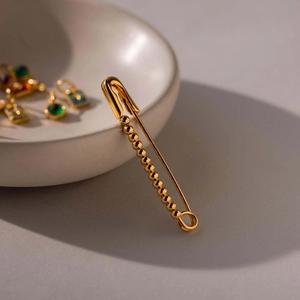 Elegante broche de imperdible dorado con cuentas decorativas en un cuenco cerámico