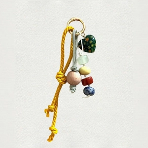 Detail of bohemian bag charm with colorful beads, yellow cord, and green heart pendant