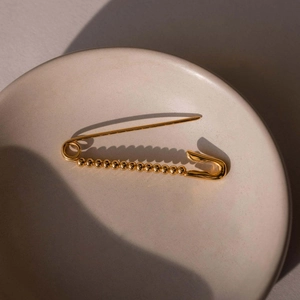 Elegante broche de imperdible chapado en oro con cuentas en una bandeja de cerámica