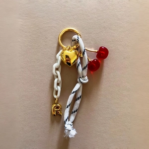 Detail of keychain with gold heart, white chain, and red cherry charms on rope link