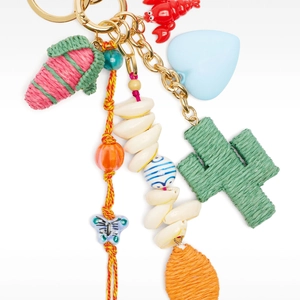 Macro view of a colorful bag charm with woven cactus, shell, and gold-tone metal clips