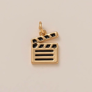Detalle macro de un colgante de claqueta de cine bañado en oro 18K con esmalte negro
