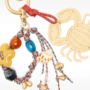 Macro view of woven straw crab pendant with colorful beads and golden charms on handbag