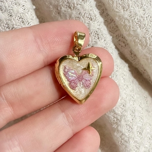 Détail d'un médaillon cœur en or 18K avec papillon pailleté rose et accents d'étoiles
