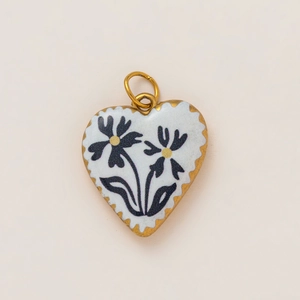 Close-up of heart pendant with 18K gold plating and black daisy enamel patterns