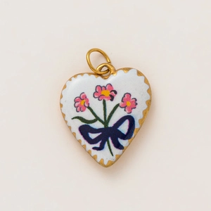 Macro detail of heart pendant with pink floral pattern and blue bow on 18K gold base