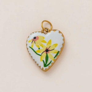 Detailed macro view of heart-shaped pendant with white enamel and yellow daisies in 18K gold