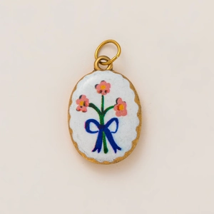 Detailed macro view of an oval 18K gold-plated pendant with pink flowers and a blue bow