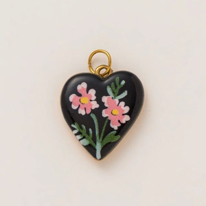 Macro detail of heart-shaped black enamel pendant with pink floral motif and 18K gold plating