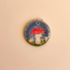 Detail of round ceramic pendant featuring hand-painted mushroom and golden dots