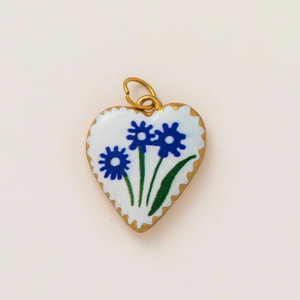 Detailed macro view of heart-shaped gold pendant with white enamel and blue flowers