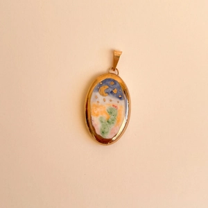 Detailed macro view of an oval 18K gold pendant featuring a hand-painted desert night scene