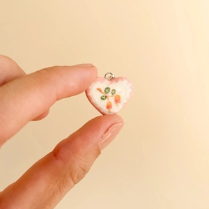 Detail of a pink heart-shaped pendant with berry floral patterns and a silver loop