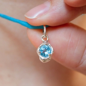 Detailansicht eines 18K vergoldeten Anhängers mit facettiertem blauem Edelstein und Farbtropfen