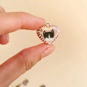Macro detail of pink heart pendant with cat motif and gold radial stripes held by fingers