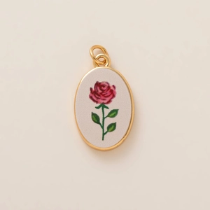 Dettaglio macro del ciondolo ovale in oro con motivo di rosa rossa su sfondo avorio