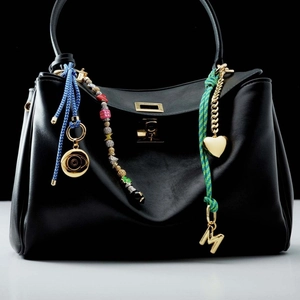 Close-up of colorful DIY bubble letter M pendant and charms on a black leather handbag