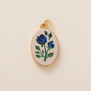 Dettaglio del ciondolo ovale dorato con rosa blu smaltata e stile vintage