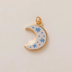 Macro shot of gold-plated crescent moon pendant with blue stars and cream enamel finish