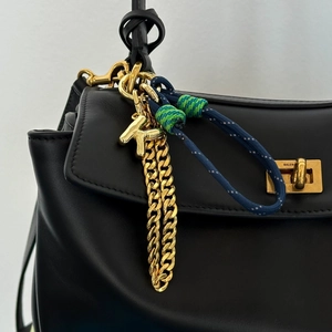 Close-up of golden letter K charm with colorful braided rope on a black leather bag