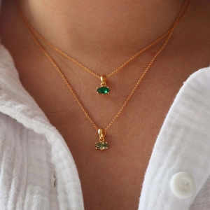 Detail of layered gold necklaces with marquise-cut emerald and light green gemstone pendants