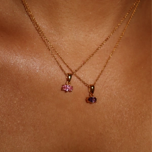 Close-up of elegant gold necklaces featuring pink and purple marquise gemstone pendants