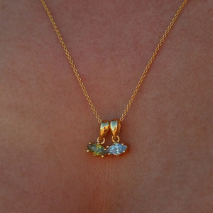 Detail of model wearing a gold chain with marquise-cut green and clear gemstone pendants