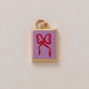 Macro detail of a gold rectangular pendant with purple enamel and a red bow charm