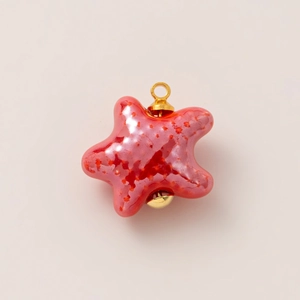 Detalle de un colgante de cerámica en forma de estrella con esmalte rosa y aro dorado