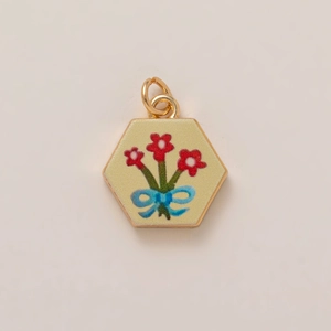 Detailed close-up of a hexagonal gold-plated pendant with red flowers and blue bow