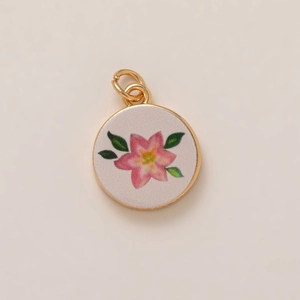Detail view of a round gold-plated pendant featuring hand-painted pink flowers and green leaves