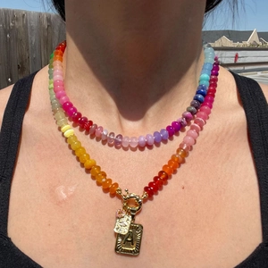 Detail of a colorful beaded double-layer necklace with a golden letter A pendant on a model