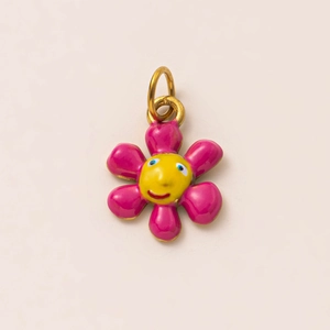 Macro view of flower-shaped charm with pink petals, yellow smiley face and 18K gold ring