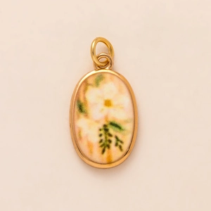 Detalle de un colgante ovalado vintage con marco dorado y diseño floral pintado a mano