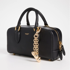 Elegant black leather satchel with golden Coach logo and heart charm chain accessory