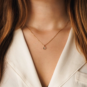 Dettaglio di una delicata collana con ciondolo a fiore dorato indossata da una modella