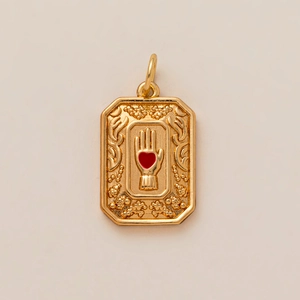 Vue macro d'un pendentif rectangulaire doré avec main en relief et détail de cœur rouge