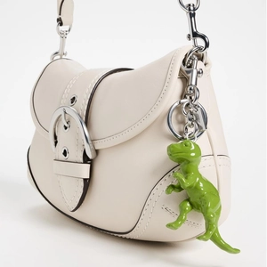 Detail of cream leather saddle bag featuring silver buckle and green dinosaur charm