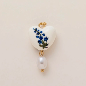 Detail of heart pendant with blue floral patterns and hanging white pearl charm