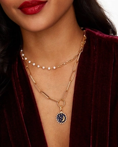 Detail of layered gold necklace with pearl accents and blue enamel moon star coin pendant