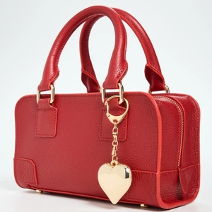 Detail of red pebbled leather handbag with gold zipper and heart-shaped metal pendant